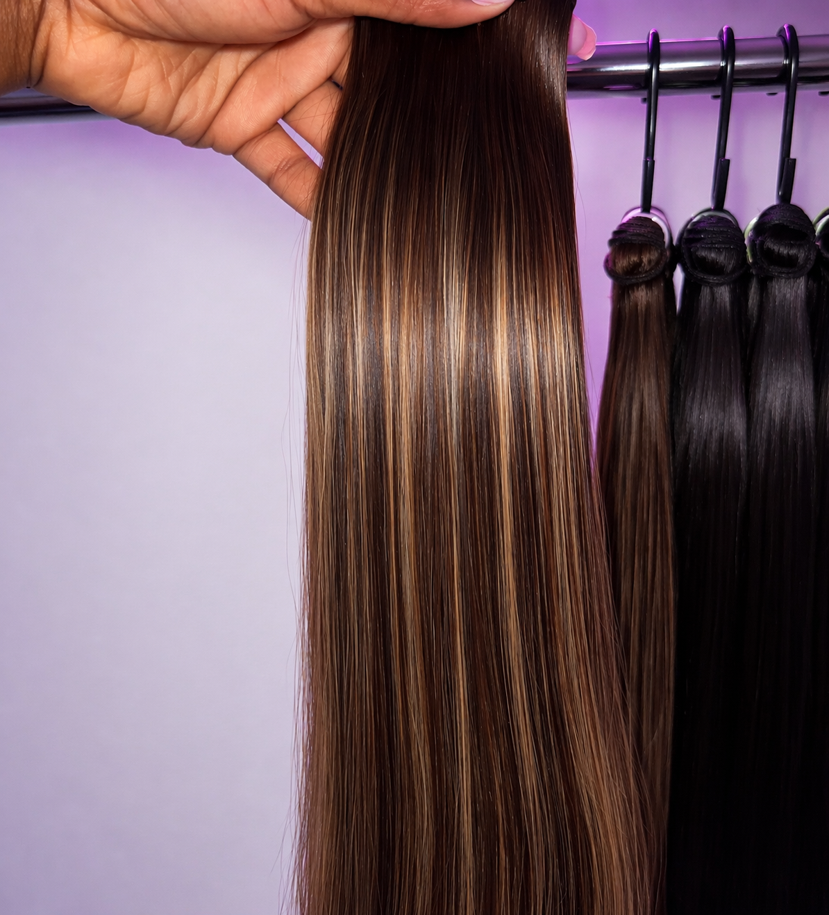 Brown hair extensions held by a hand with a purple background
