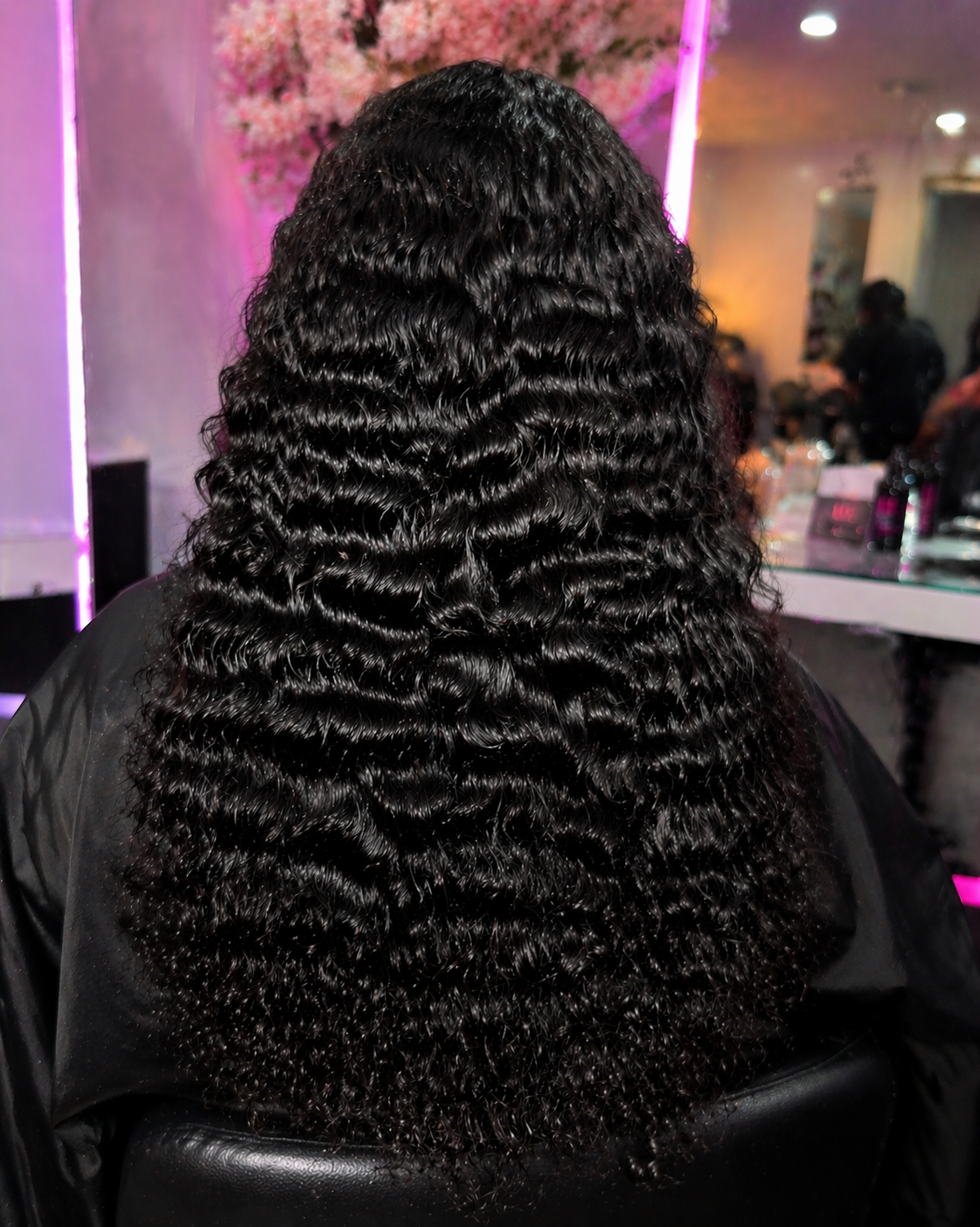 Person with a long  black burmese curly wig sitting in a salon chair.